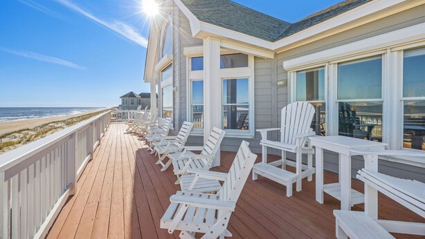 Une terrasse en bois avec des chaises Adirondack blanches et vue sur la plage.