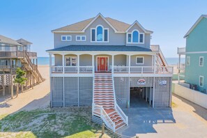Une maison située en bord de mer, dotée d’un balcon, d’une porte rouge et d’un escalier menant à l’entrée.