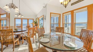 Un espace repas comprenant une table à plateau en verre, des chaises en bois et de grandes fenêtres donnant sur l’océan.