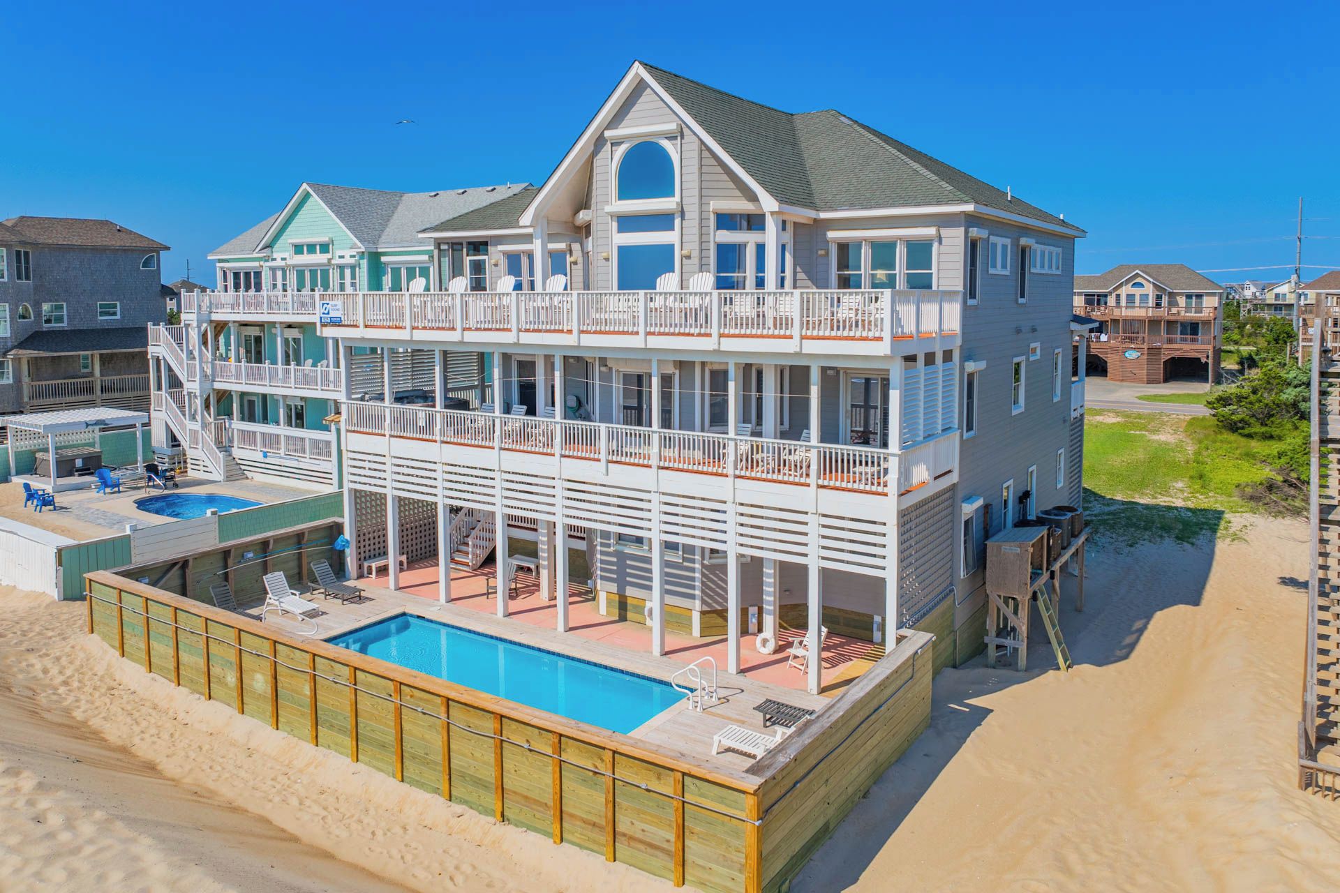 A multi-story beachfront property with a swimming pool, balconies, and a beach access ramp.
