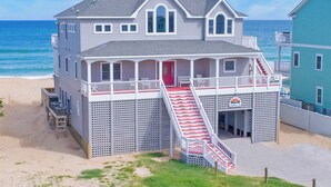 Un hôtel de deux étages situé en bord de mer, avec une porte rouge, des balustrades blanches et un escalier menant à l’étage supérieur.