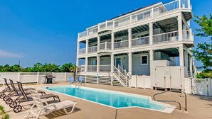 A two-story building with a pool area, including lounge chairs and a lifeguard stand. - Soundside Home w/ Private Pool, Hot Tub, Game Room, Cabana, Community Boat Ramp (Salvo)
