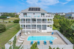 A multi-story building with a rooftop solar panel, a swimming pool, and a fenced deck area with lounge chairs.