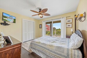 A bedroom with a bed, a ceiling fan, a sliding glass door to a balcony, and a television on a stand.