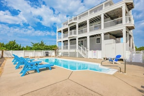 A pool area with a multi-level building, a pool, and lounge chairs.