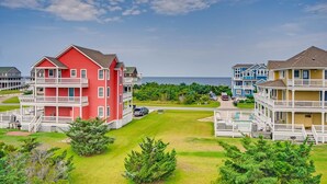 A coastal residential area with multi-story buildings, a grassy lawn, and a view of the sea. - Soundside Home w/ Private Pool, Hot Tub, Game Room, Cabana, Community Boat Ramp (Salvo)