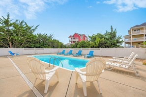 A swimming pool with lounge chairs and a white fence.
