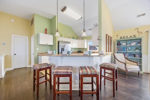 Une cuisine avec un îlot central, des tabourets de bar, une bibliothèque et un panneau « RELAX » accroché au mur.