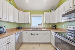 Une cuisine avec des meubles blancs, une fenêtre, un grille-pain, une machine à café et une cuisinière.
