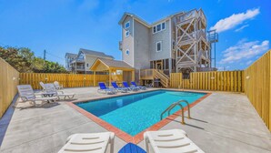 A swimming pool with lounge chairs, a wooden deck, and a multi-story building with a balcony. - Oceanview w/ Private Pool, Hot Tub, Game Room, and Wet Bar. Surf's Up Rodanthe! (Rodanthe)