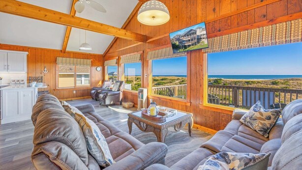 A spacious living room with a large sofa set, a dining area, and a view of the beach.