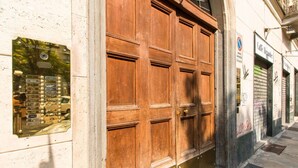 A large wooden door with a plaque on the left, a metal plaque on the right, and a sign above the door. - GuestHost - Studio apartment 5 minutes from the Mole and Royal Gardens! (Torino)