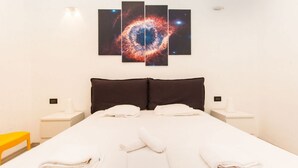 A hotel room with a large bed, two pillows, a nightstand with a lamp, and a wall-mounted galaxy artwork. - GuestHost - Studio apartment 5 minutes from the Mole and Royal Gardens! (Torino)