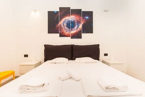 A hotel room with a large bed, two pillows, a nightstand with a lamp, and a wall-mounted galaxy artwork.