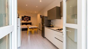 A modern kitchen with white cabinets, a stainless steel refrigerator, and a dining area with a table and chairs. - GuestHost - Studio apartment 5 minutes from the Mole and Royal Gardens! (Torino)