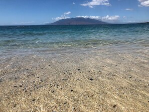 A clear beach with visible pebbles and a mountain in the distance.