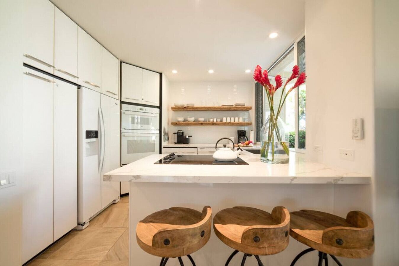 A modern kitchen with white cabinetry, a central island, and wooden bar stools.