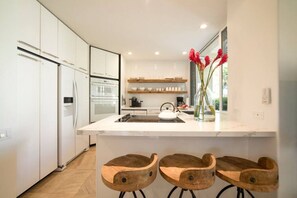 A modern kitchen with white cabinetry, a central island, and wooden bar stools.