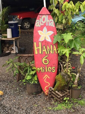 A red surfboard-shaped sign with 'Hana 6 Miles' and a flower symbol, surrounded by potted plants and a red vehicle in the background. - ContemporaryHawaiianReno in Wailea*Pool*Beach*Golf (Wailea)