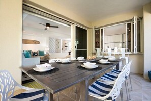 A dining area with a long table set for six, white chairs, and a view into the living room.
