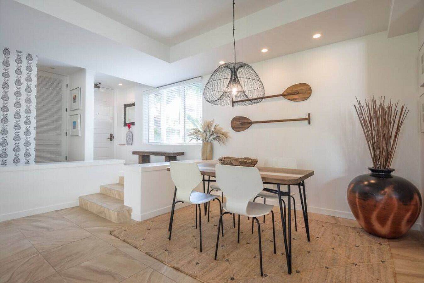 A dining area with a wooden table, two chairs, a hanging light fixture, and a decorative wall piece.