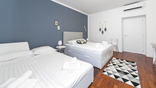 A hotel room with two beds, a white door, and a geometric patterned rug.