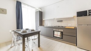 A modern kitchen with a dining table, chairs, a stove, oven, and a refrigerator.
