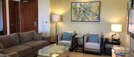 A living room with a glass coffee table, two armchairs, a sofa, a floor lamp, and a painting on the wall.
