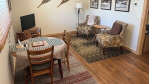 A cozy living room with a dining area, featuring a TV, a table with chairs, a lamp, and three framed pictures on the wall. - Adults 25 plus Only, Creekside Vacation Rental 1, Downtown Historic CITY APPROVE (Buffalo)