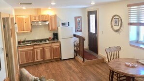 A compact kitchen with wooden cabinets, a white refrigerator, and a microwave. There's a dining area with a wooden table and chairs. - Adults 25 plus Only, Creekside Vacation Rental 1, Downtown Historic CITY APPROVE (Buffalo)