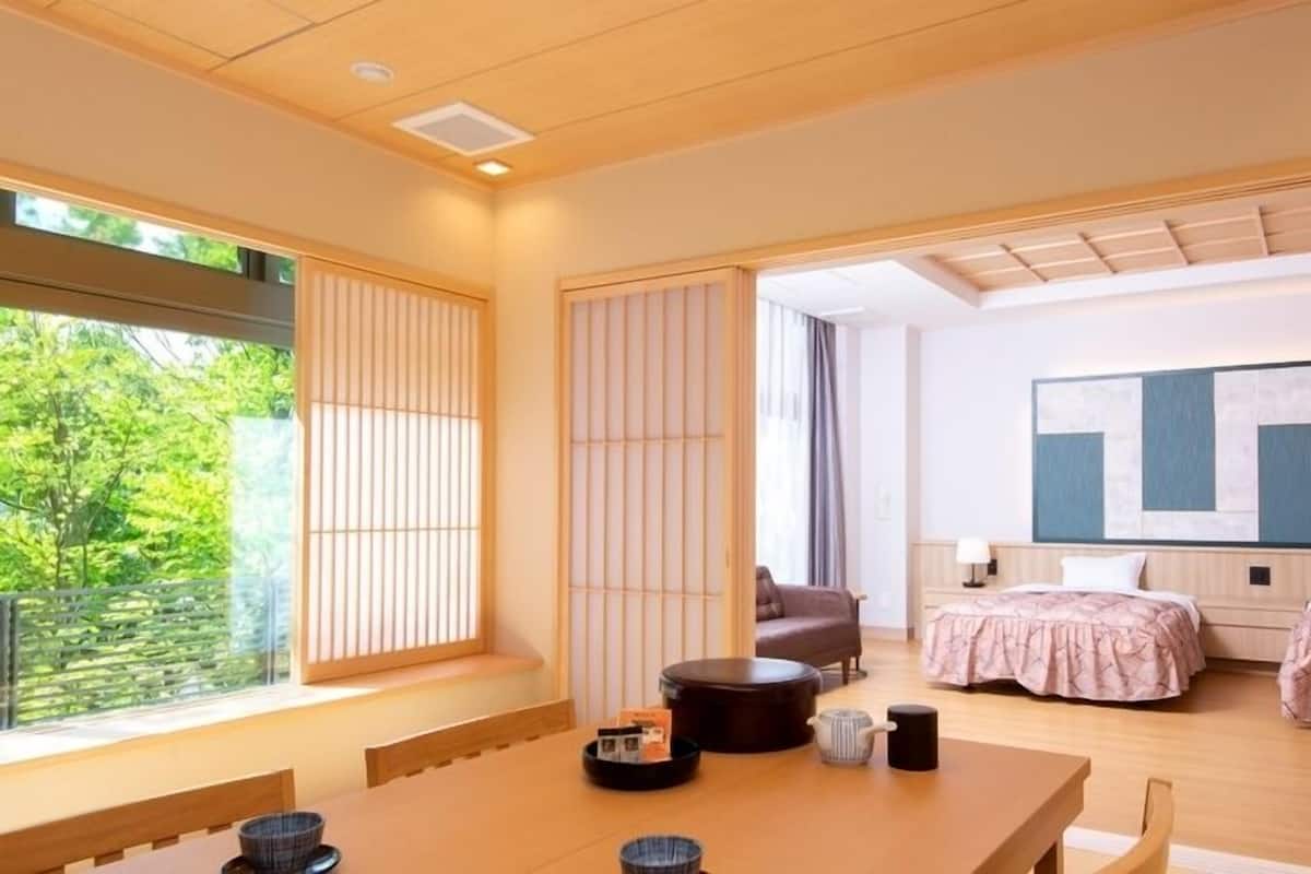 A modern hotel room with a large window, a dining area, two beds, and a large abstract painting on the wall.