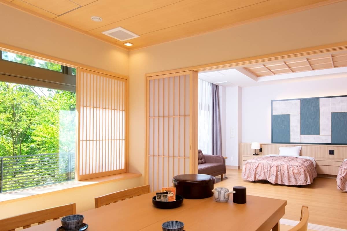 A modern hotel room with a large window, a dining area, two beds, a sofa, and a large abstract painting on the wall.