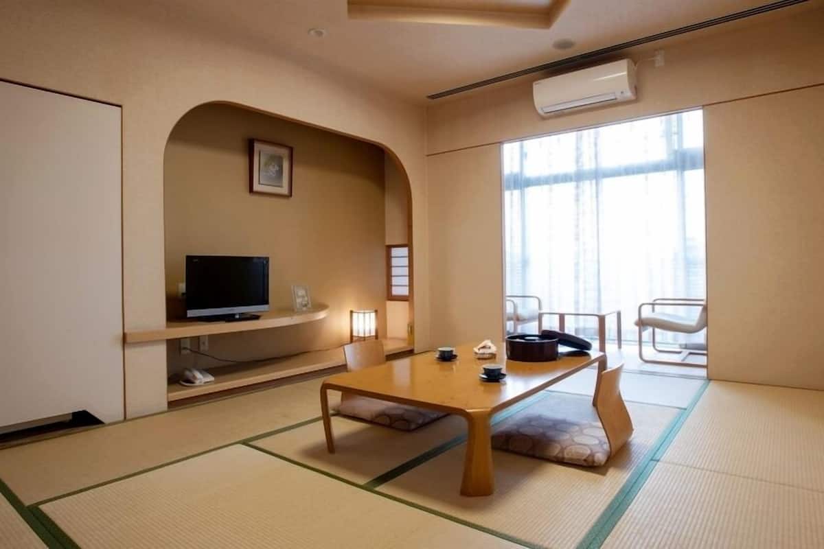 A room with tatami flooring, a television on a shelf, a table with chairs, and a large window.
