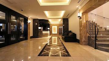 Um hall de hotel com piso de mármore, balcão de recepção, escada e um sofá.