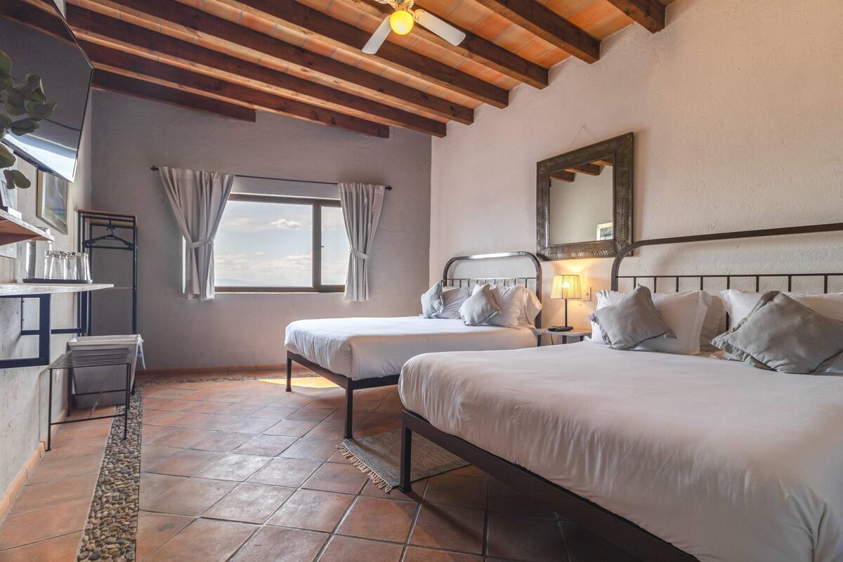 A bedroom with two beds, a window with curtains, a ceiling fan, and a mirror on the wall.