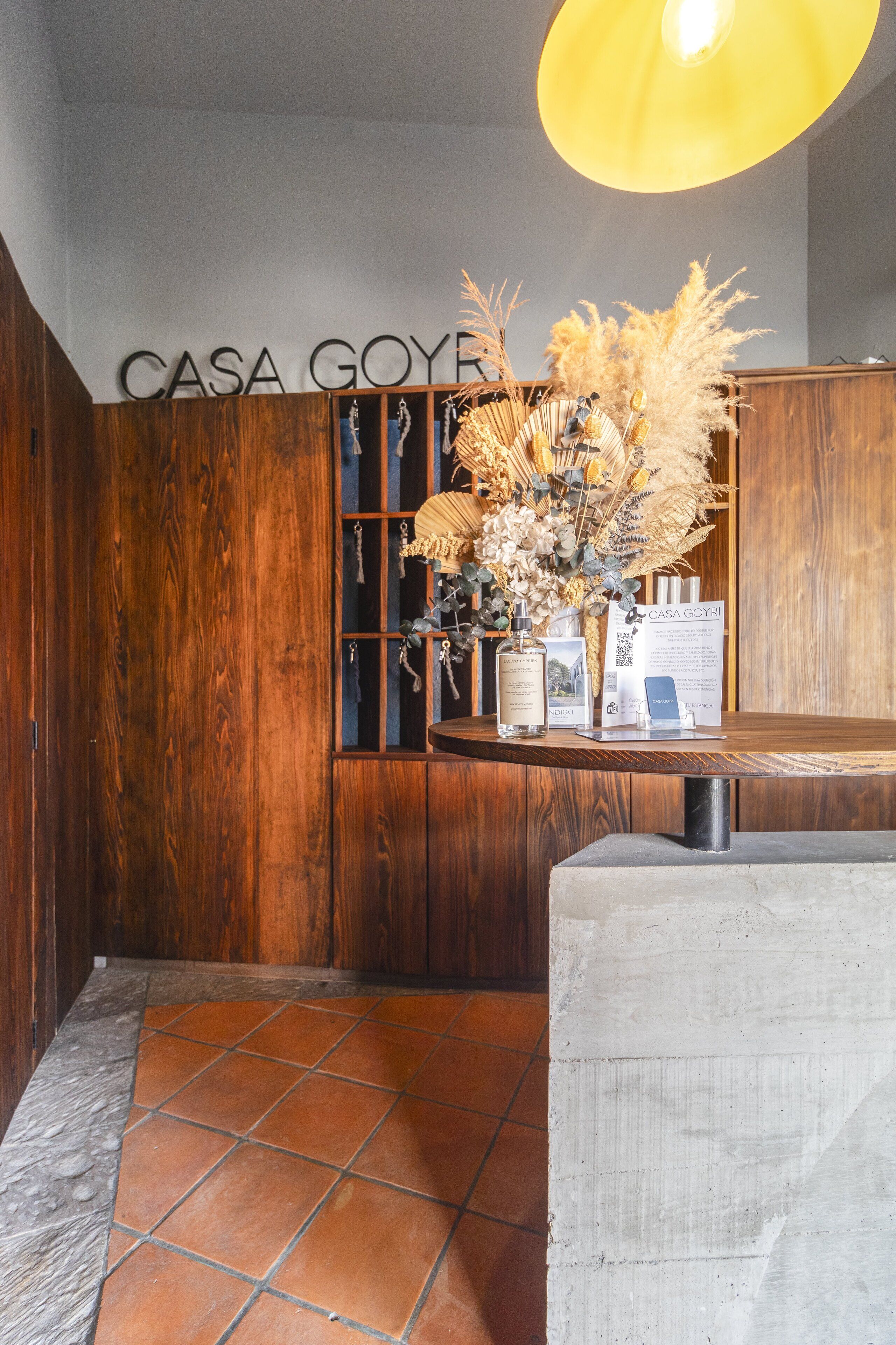 Un mostrador de recepción de madera con un jarrón de plantas secas, un código QR y un cartel que dice "CASA GOY".