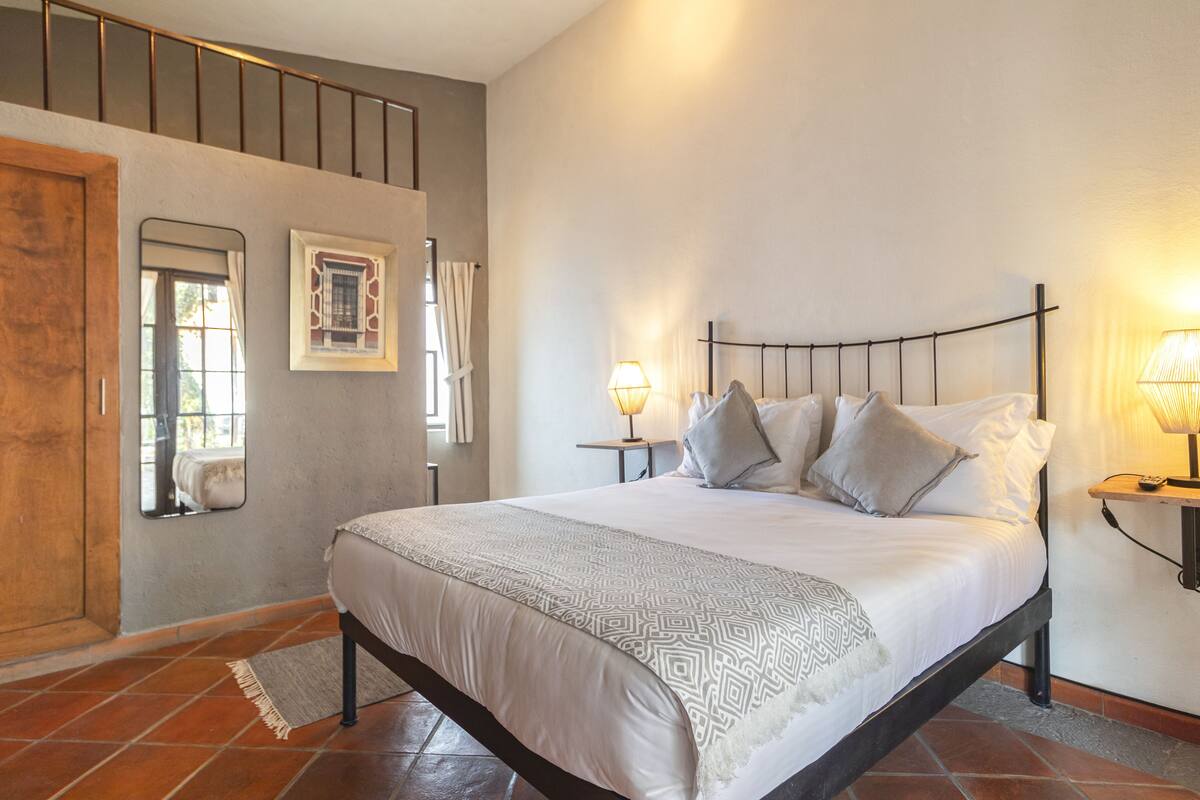 A bedroom with a bed, two bedside tables, a window, and a door.