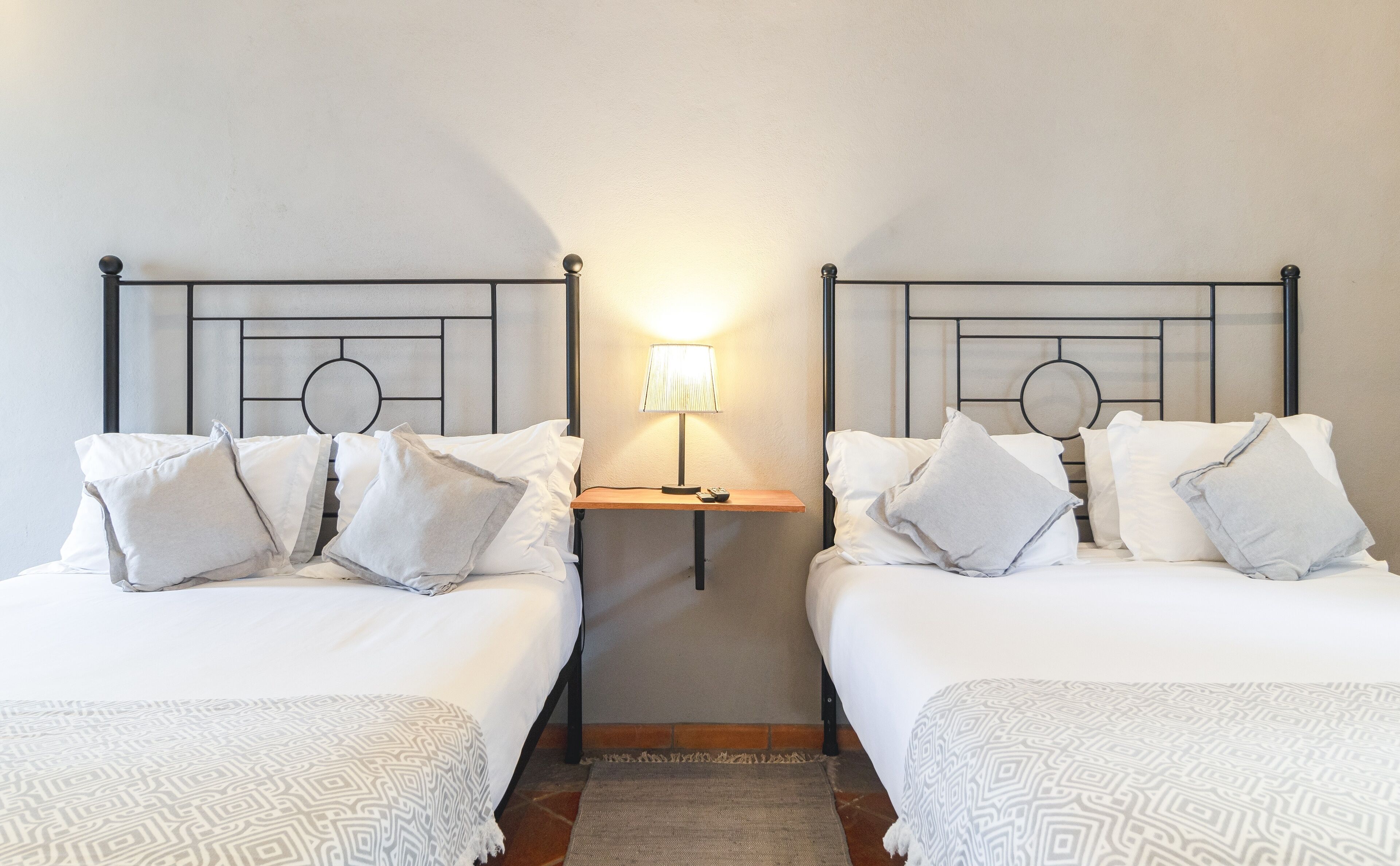 A hotel room with two beds, a nightstand with a lamp, and a patterned rug.