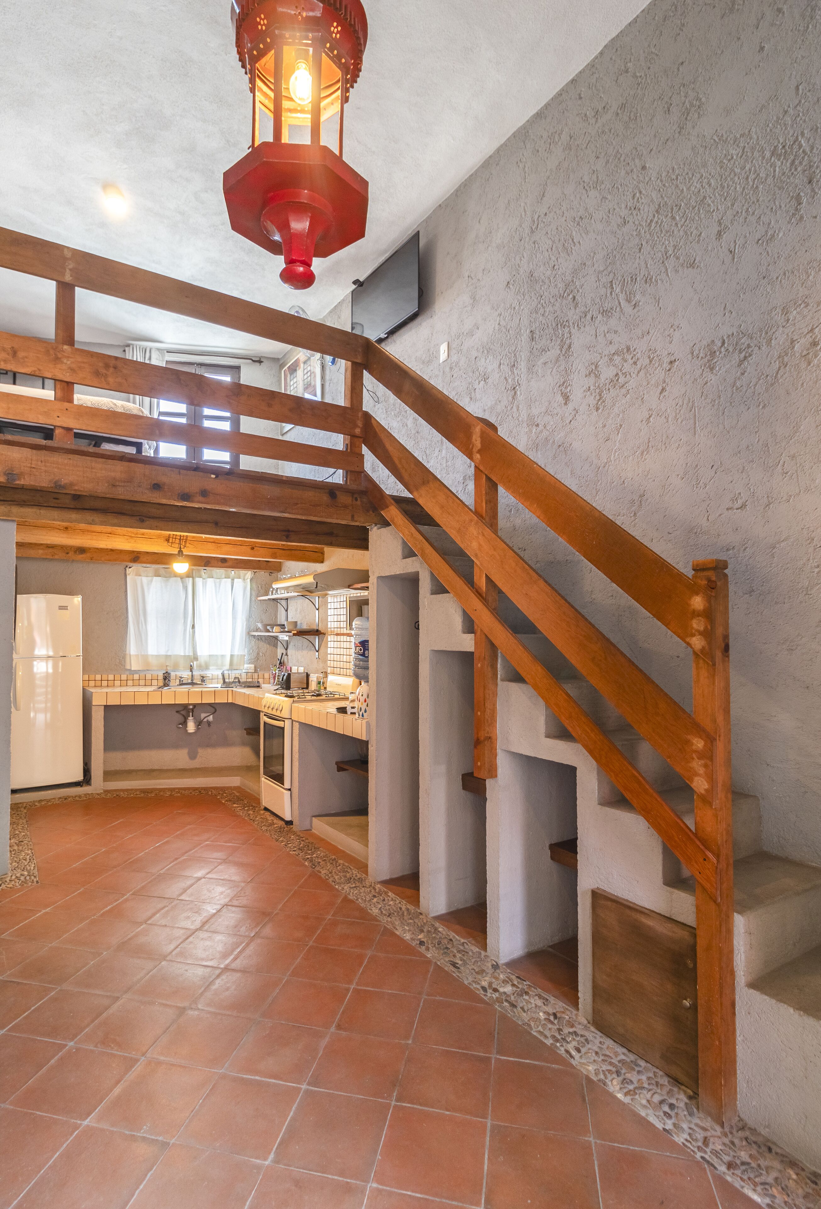 Una cocina rústica con una escalera de madera, un farol rojo y suelo de baldosas.