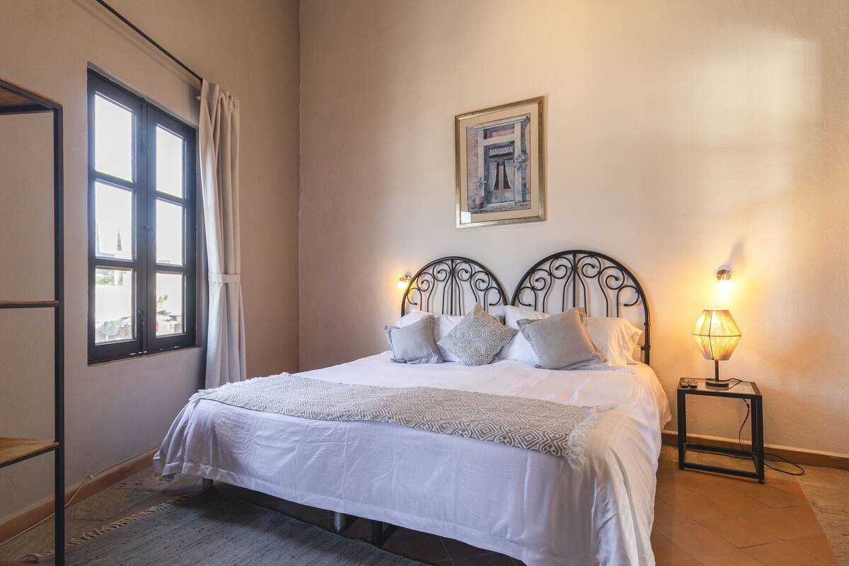 A neatly made bed with a patterned bedspread, a bedside lamp, and a framed picture on the wall.