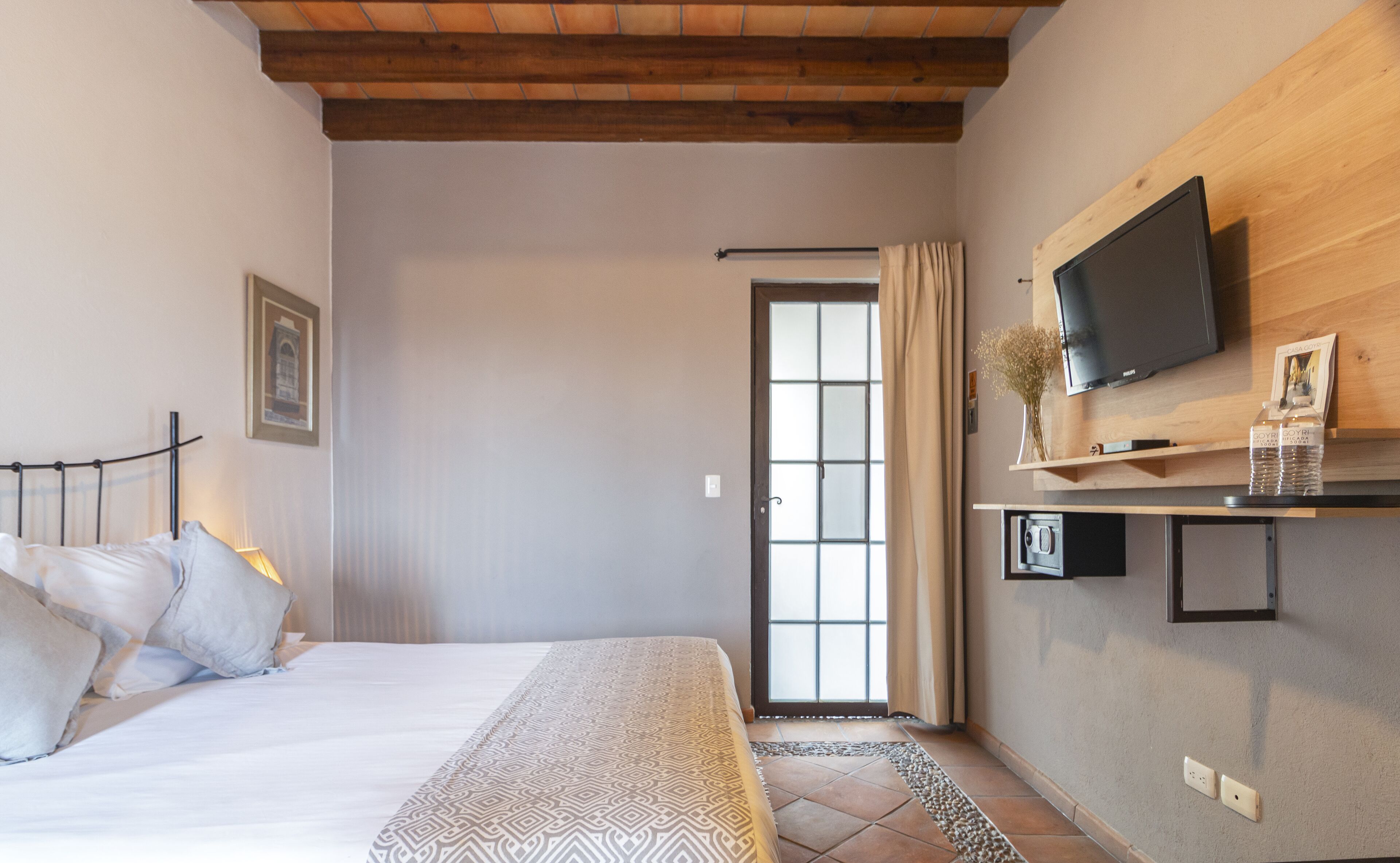 A bedroom with a bed, a television mounted on the wall, and a door leading to another room.