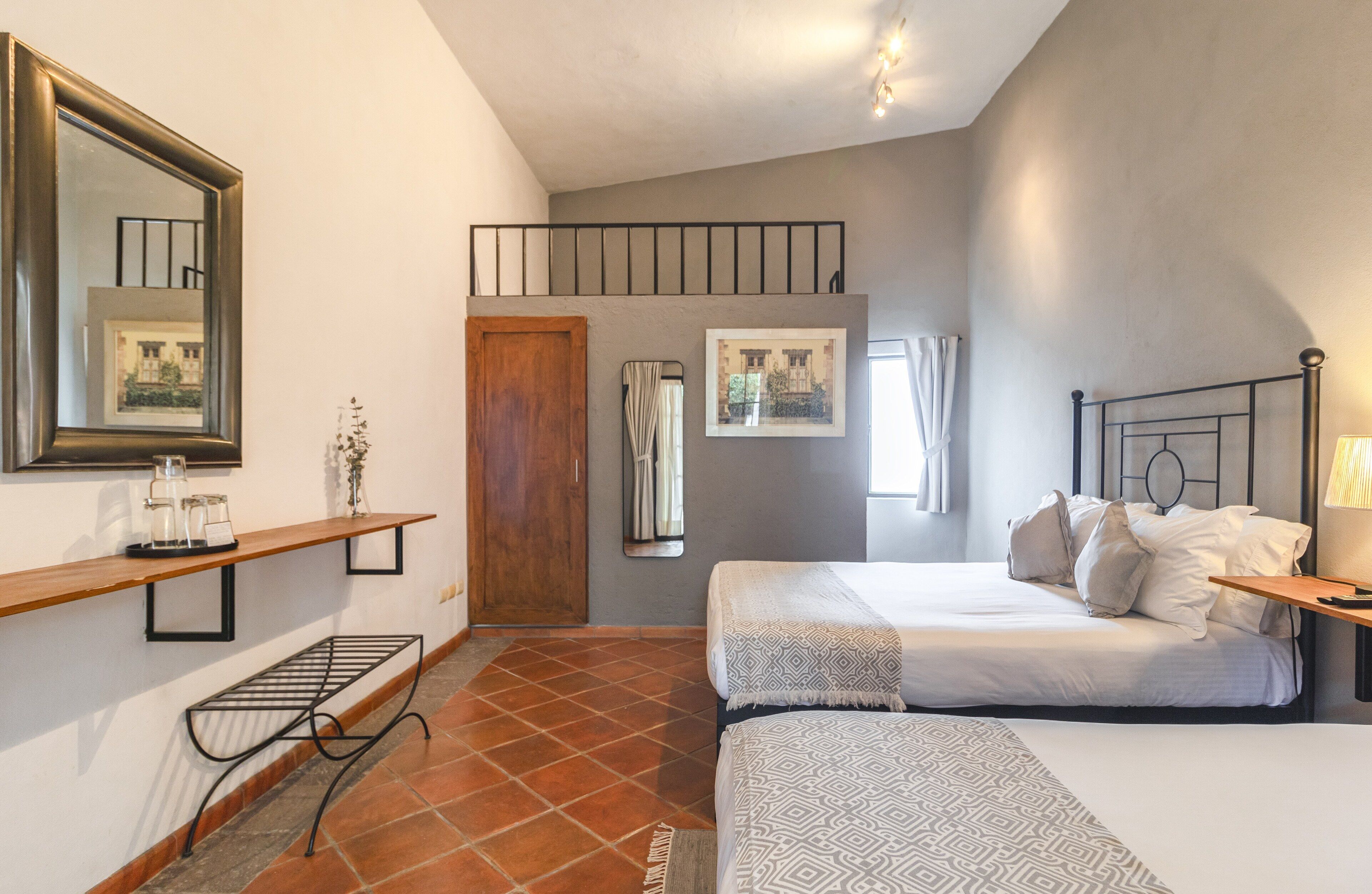 Une chambre avec deux lits, une étagère en bois avec des bocaux en verre, un miroir et une porte donnant sur un balcon.