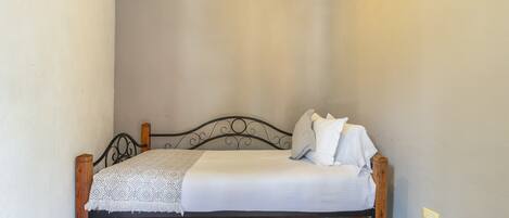 A single bed with a wooden headboard, white bedding, and a patterned throw blanket.