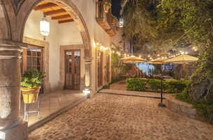 A cobblestone courtyard with outdoor seating, stone columns, and string lights.
