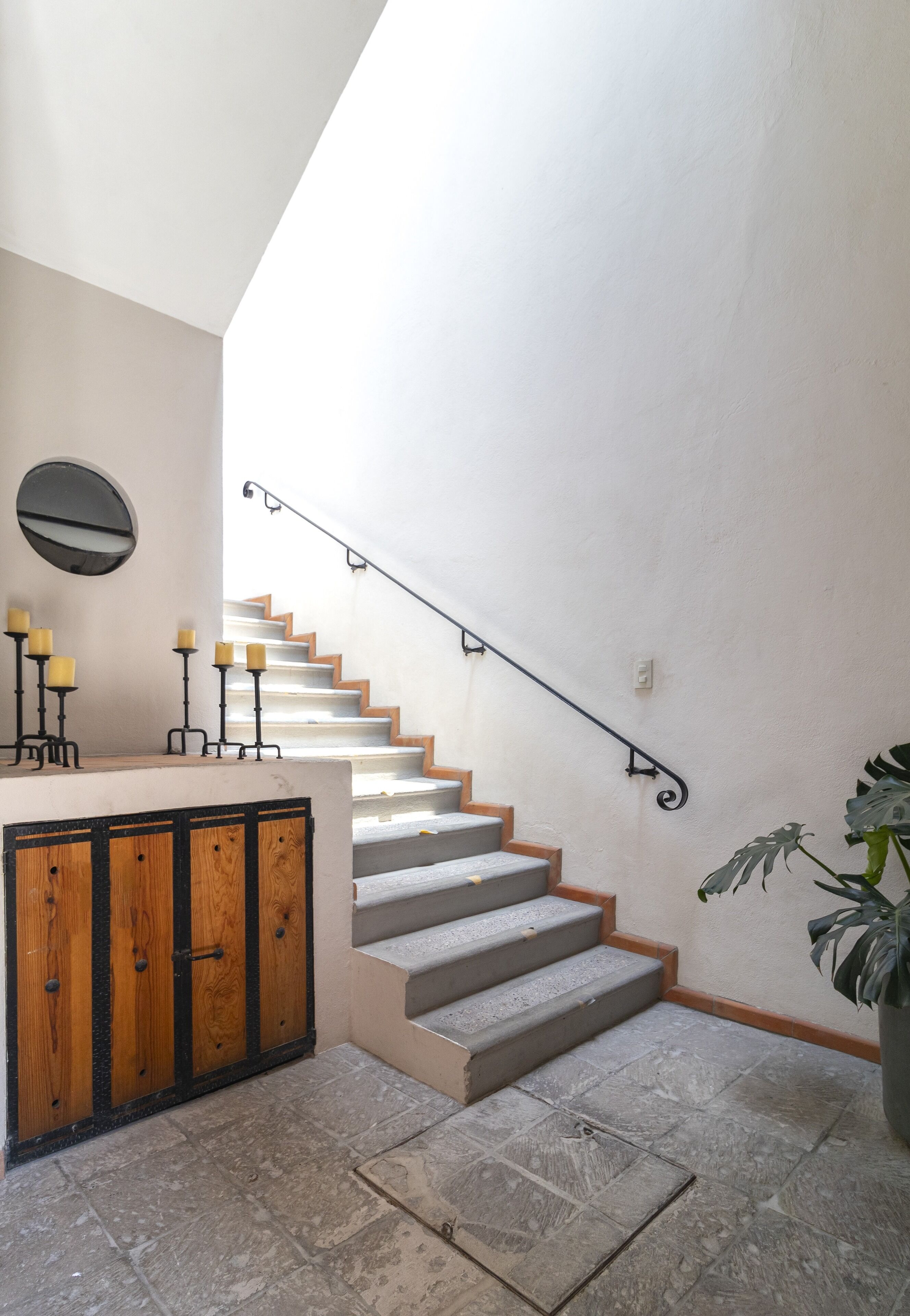 A staircase with a handrail, a wooden cabinet with candles, and a potted plant.