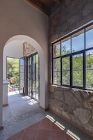 An interior corridor with stone walls, a tiled floor, and a large window with a view of greenery outside.