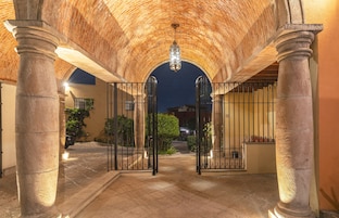 An arched entrance with stone columns and a metal gate, leading to a building with a brick facade.