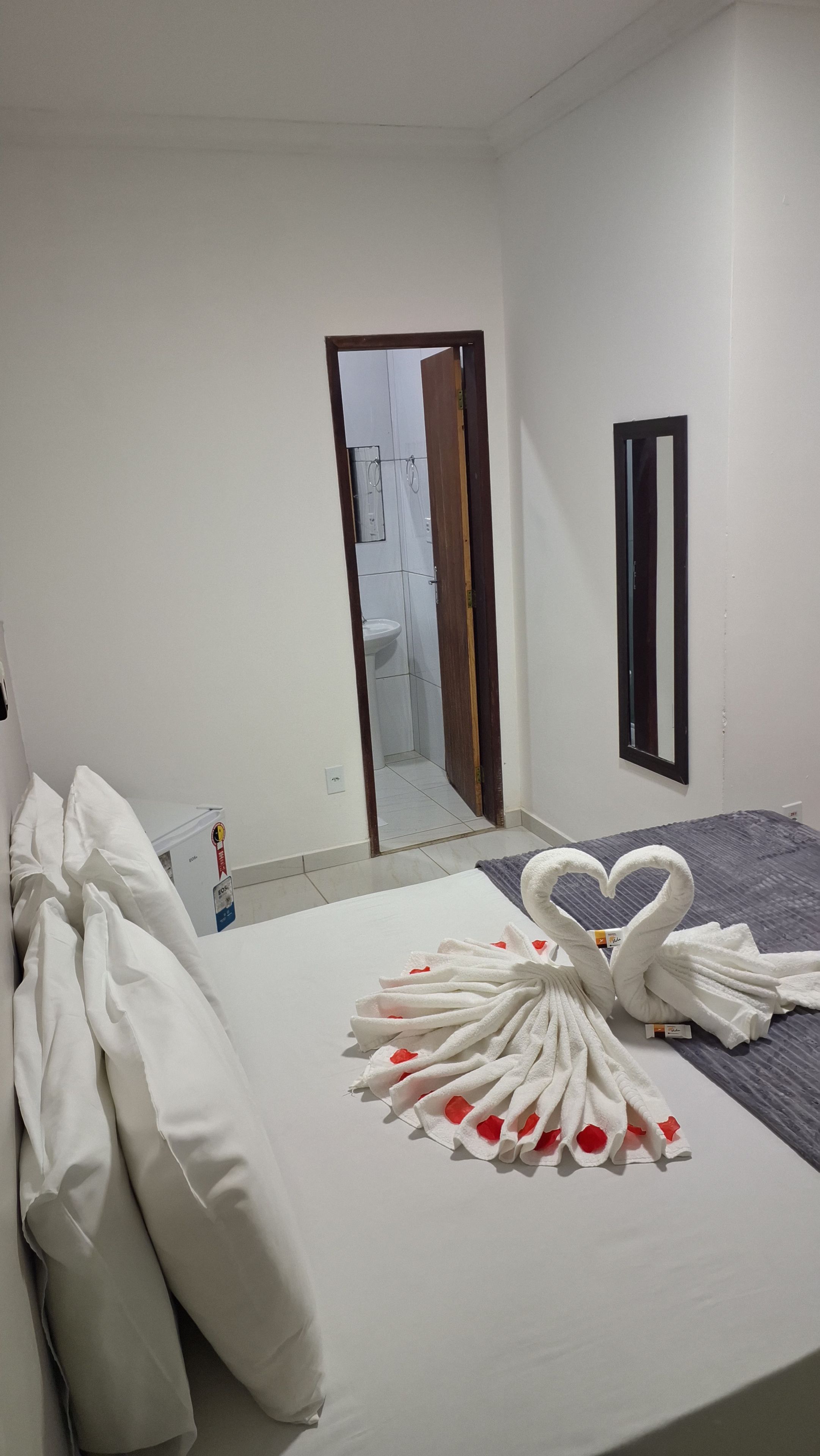 A hotel room with a bed, pillows, a towel arrangement, a mirror, and a bathroom visible through an open door.