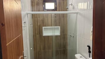 Casa de banho com chuveiro separado por vidro, sanita, bidé e lavatório.