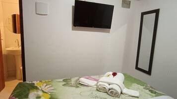 Habitación de hotel con cama, televisión, aire acondicionado, espejo y baño visible a través de una puerta abierta.